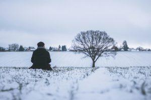 A person in a snowy landscape next to a lonely tree, signifying loneliness even at Christmas.